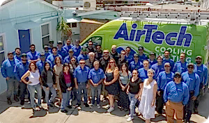 %Focuskw% | Airtech A large group of people, some in blue AirTech uniforms, pose together in front of a green AirTech Cooling & Heating van outside a building.