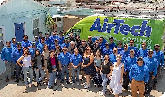 %Title% | Airtech A large group of people, some in blue AirTech uniforms, pose together in front of a green AirTech Cooling & Heating van outside a building.